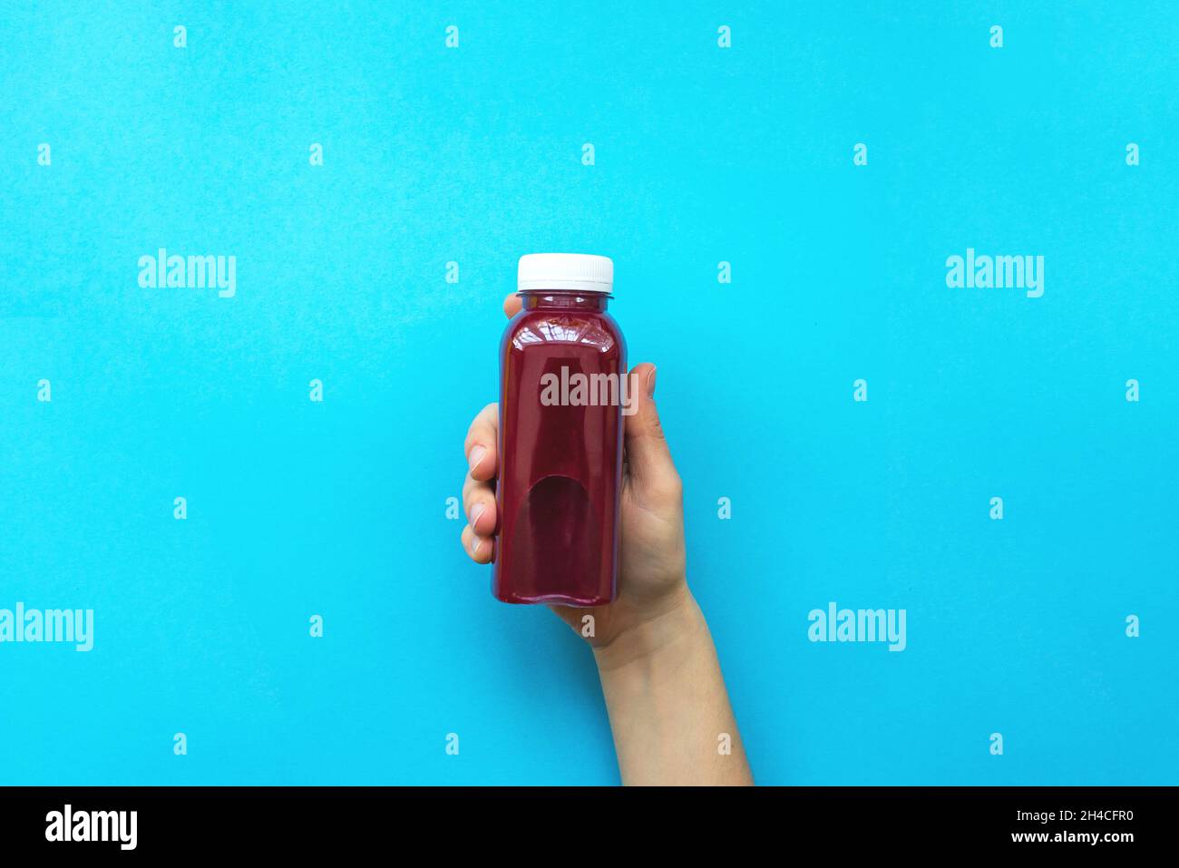 Le mani femminili tengono bottiglie di plastica con succo o frullato rosso su sfondo blu. Il concetto di diete, disintossicazione Foto Stock