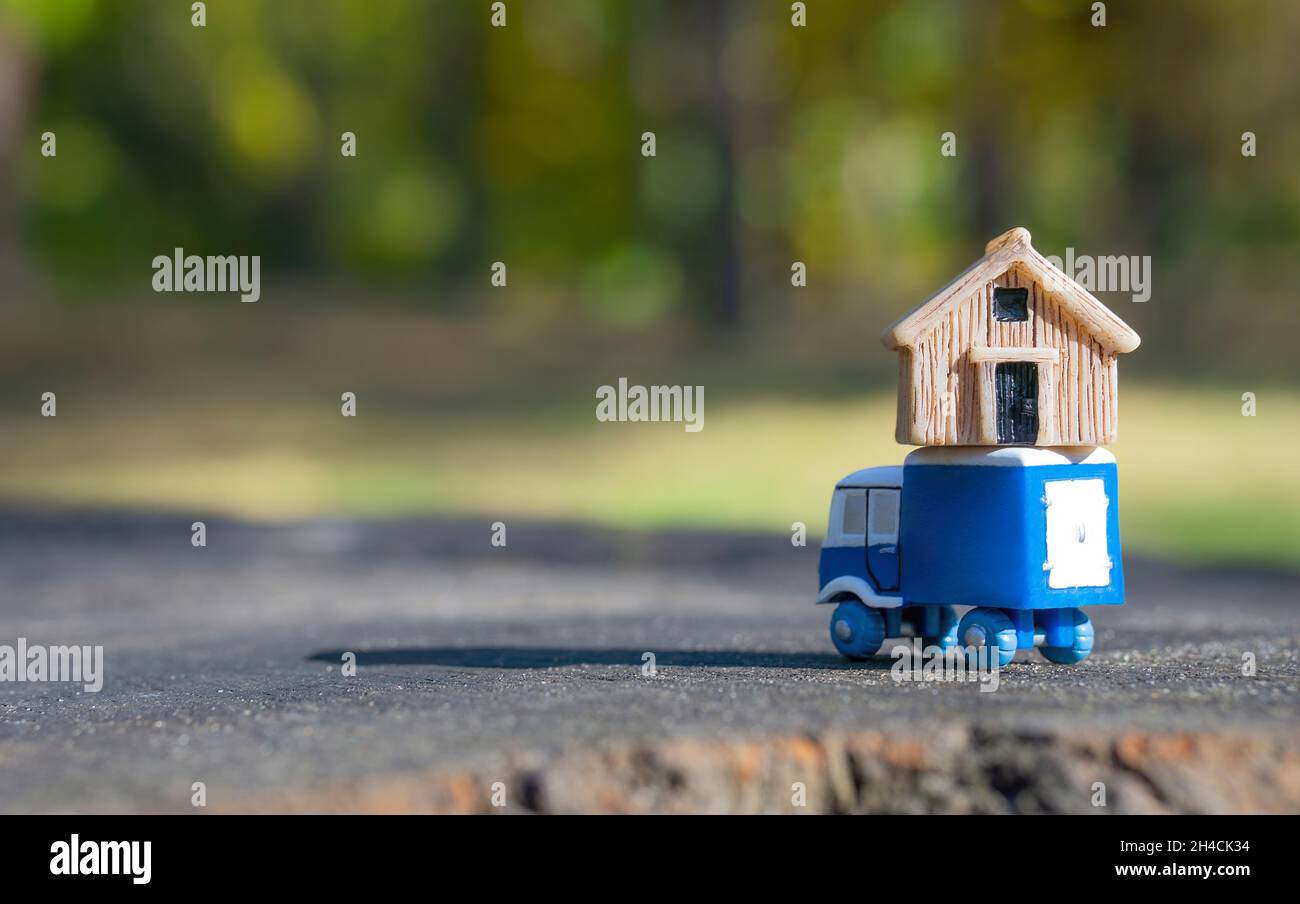 Primo piano di un piccolo camion giocattolo che trasporta una piccola casa sulla parte superiore contro uno sfondo sfocato della foresta. Messa a fuoco su primo piano, spazio di copia. Trasferimento rurale conc Foto Stock