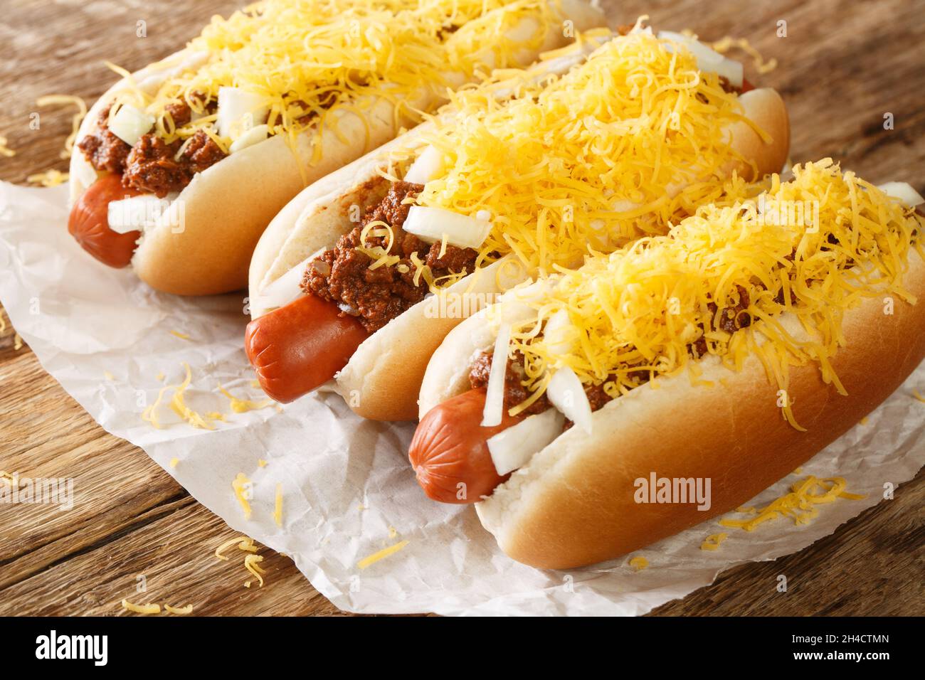 Hot dog di Cincinnati Chili con salsiccia di manzo, formaggio cheddar e cipolle in primo piano nel foglio sul tavolo. Orizzontale Foto Stock