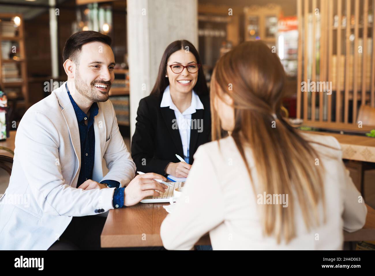 Giovani economisti che discutono di piani futuri e nuove idee in un caffè moderno, sorridendo e contenti Foto Stock