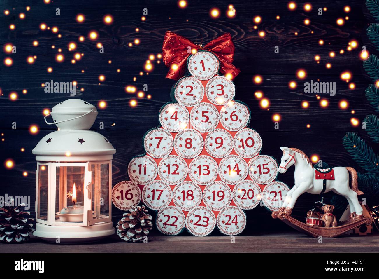 Calendario dell'avvento in forma di albero di Natale con numeri e nastro invece di stella, lampada con candela, giocattolo su tavola di legno Natale calendario dell'avvento concetto Foto Stock