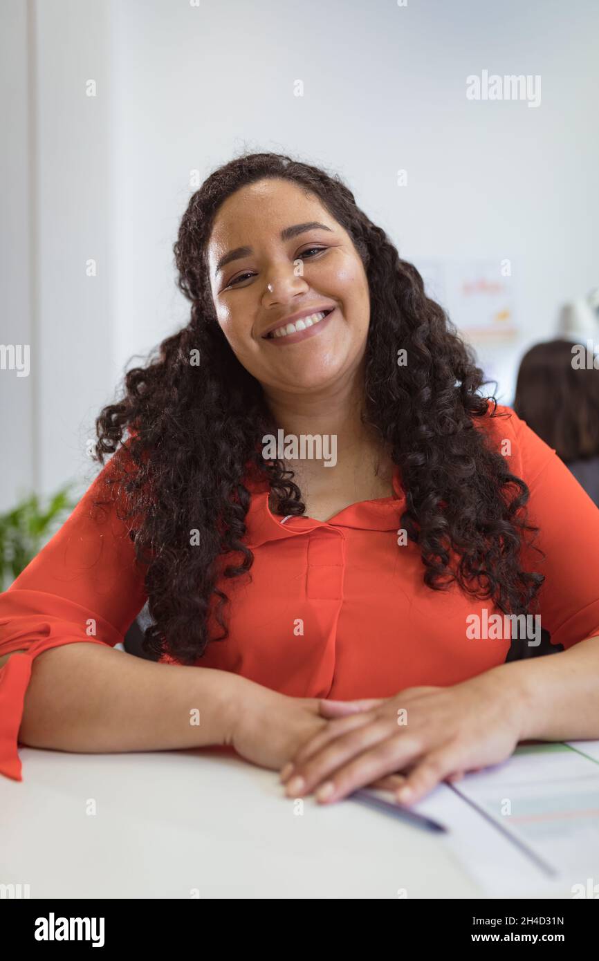 Sorridente donna d'affari biraciale seduta alla scrivania facendo videochiamata in un ufficio moderno Foto Stock