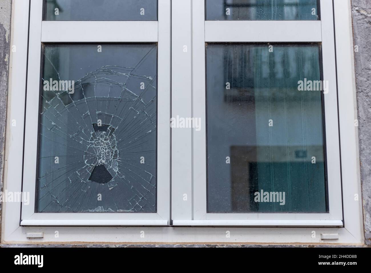 Vetro incrinato in un telaio di vetro sottovuoto in plastica. Una finestra danneggiata a causa di vandalismo, disastro naturale, o incidente. Foto Stock