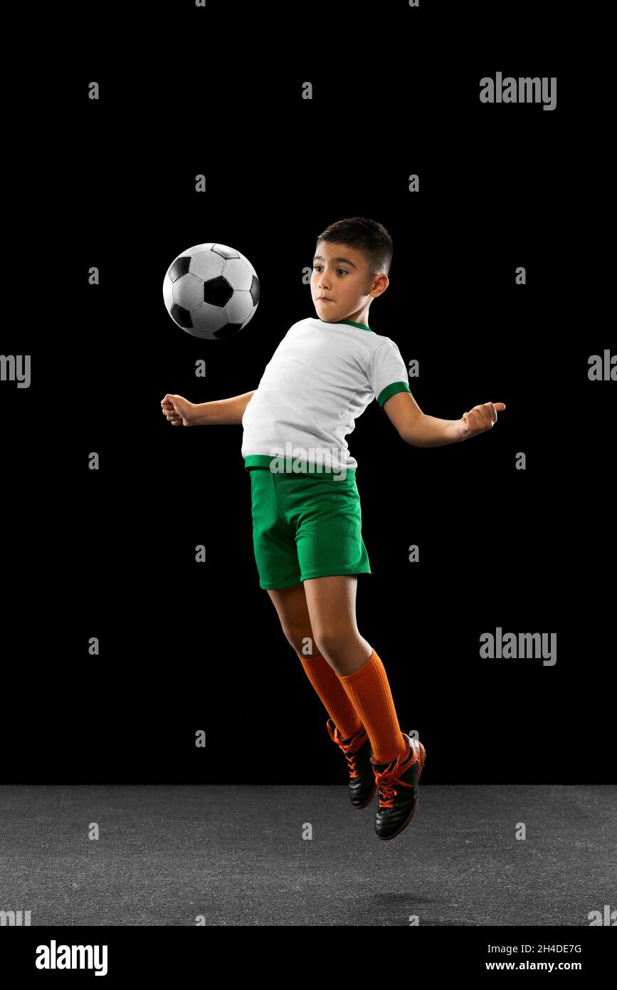 Ritratto a tutta lunghezza di ragazzo, bambino, giocatore di calcio in  uniforme allenamento, calci palla con petto in un salto isolato su sfondo  nero Foto stock - Alamy