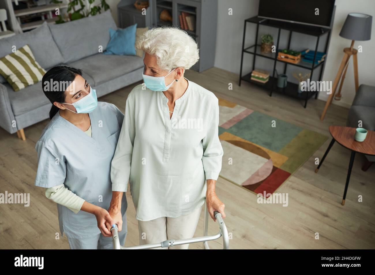 Ritratto ad angolo alto di sorridente infermiere donna che aiuta anziana con mobilità walker in casa di riposo, copia spazio Foto Stock