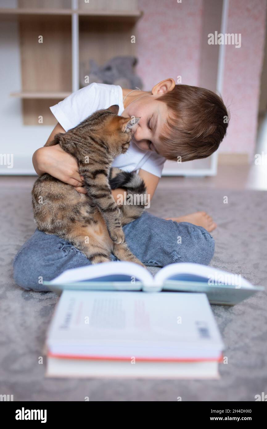 Ragazzo carino che legge un libro con un gatto. Scuola domestica. Apprendimento a distanza. Vacanze. Quarantena durante la pandemia di Coronavirus. Blocco Foto Stock
