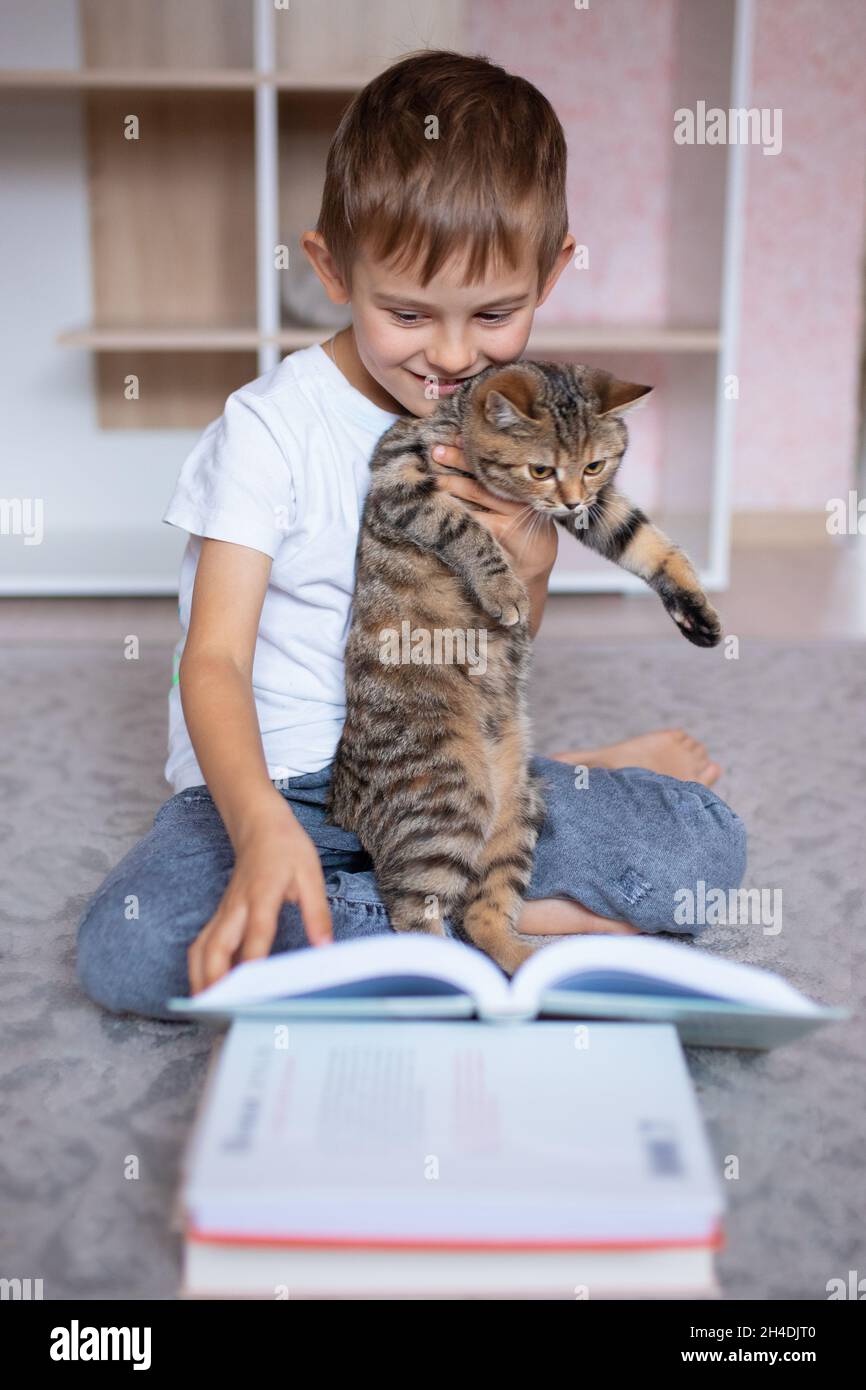 Ragazzo carino che legge un libro con un gatto. Scuola domestica. Apprendimento a distanza. Vacanze. Quarantena durante la pandemia di Coronavirus. Blocco Foto Stock