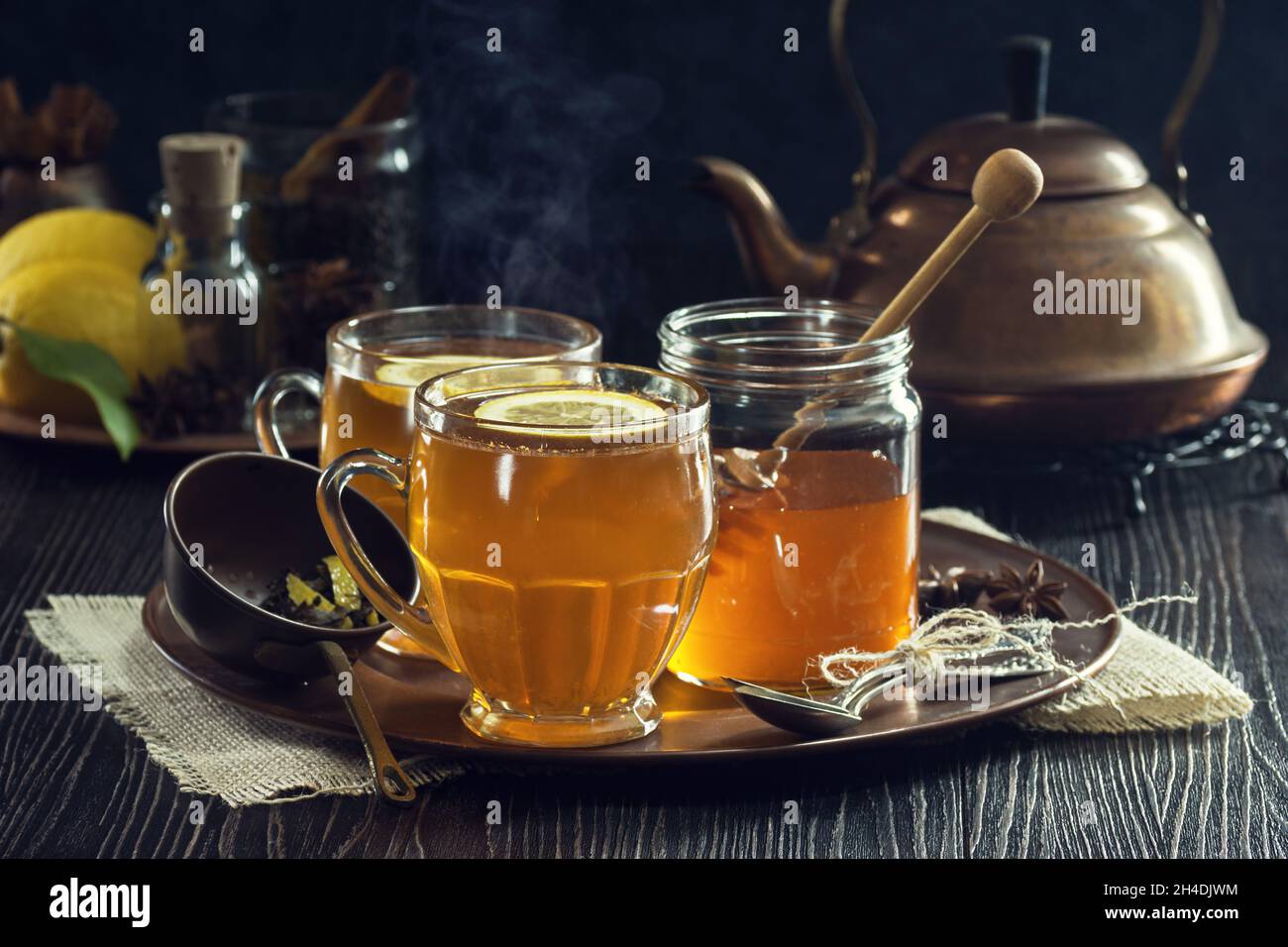 Toddie calde o tè speziato al limone con teiera di rame e ingredienti in vassoio in Agriturismo rustico scuro Foto Stock