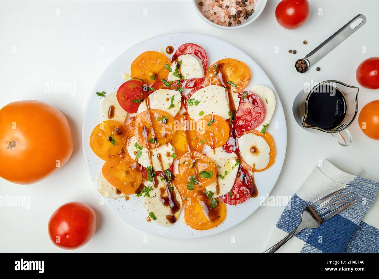 Insalata colorata con pomodori gialli rossi a fette, mozzarella, olio d'oliva, pepe e sale su sfondo bianco. Cibo vegano. Vista dall'alto. Disposizione piatta Foto Stock