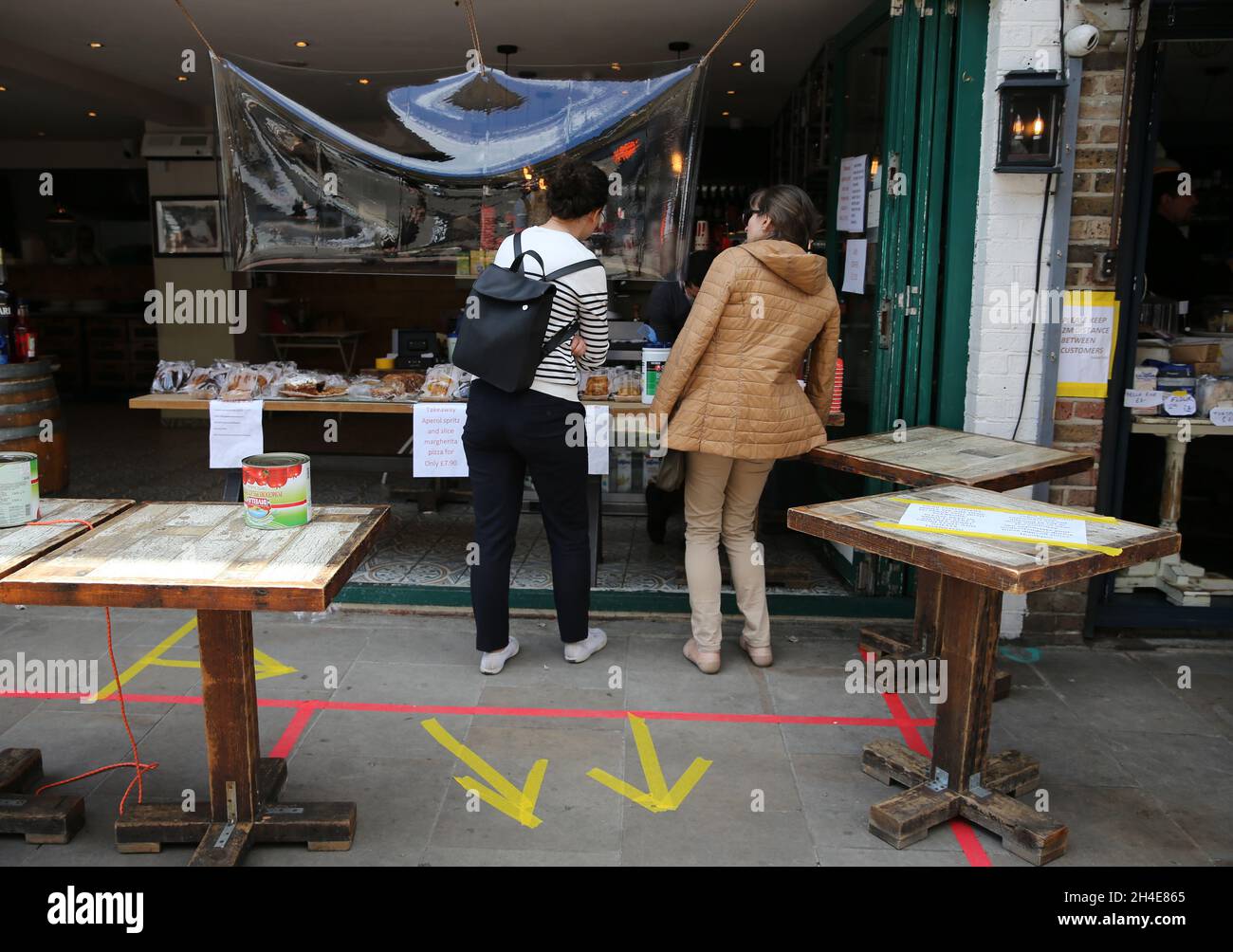 Ai clienti viene servito il caffè da un operatore dietro uno schermo di plastica, in quanto mantengono la distanza sociale sicura all'interno delle marcature del pavimento a Broadway Market, Hackney, East London, mentre il Regno Unito continua a bloccarsi per contribuire a frenare la diffusione del coronavirus. Data foto: Sabato 2 maggio 2020. Foto Stock