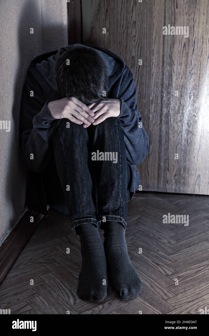 Toned Photo of Sad Teenager Sit in the Corner of the Dark Room Foto Stock