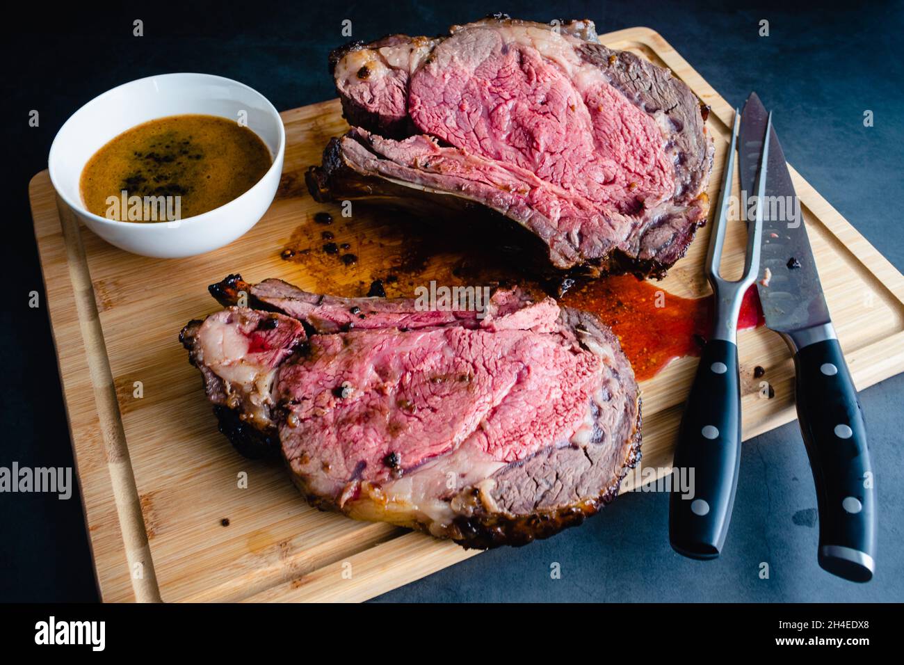 Fette di Rib Bone-in prime medio raro con Au Jus: Arrosto di costolette prime in piedi scolpito su un pannello di bambù da carving Foto Stock