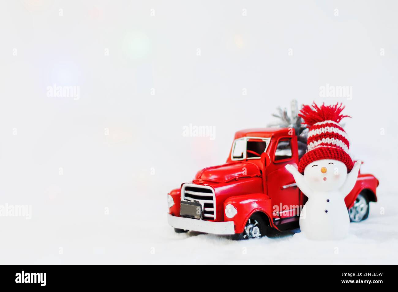 Snowman in un cappello rosso vicino rosso ritiro camion di natale, su uno sfondo bianco. Ritiro di natale buon natale e felice anno nuovo biglietto di auguri. Copia s. Foto Stock