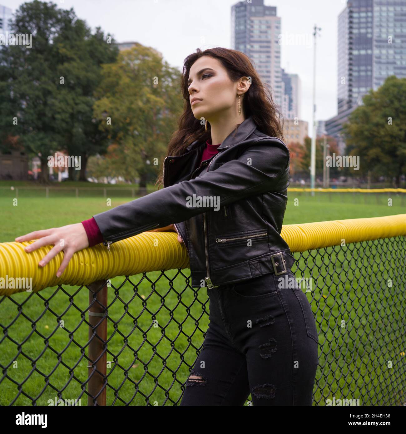 Ritratto di una giovane donna in una giacca di pelle nera in piedi di fronte a un campo da baseball Foto Stock