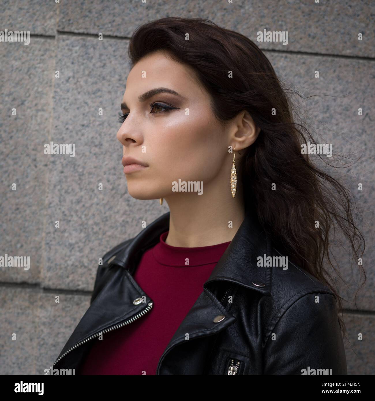 Ritratto di profilo di una giovane donna in una giacca di pelle nera che si trova di fronte ad un muro di marmo in pietra Foto Stock
