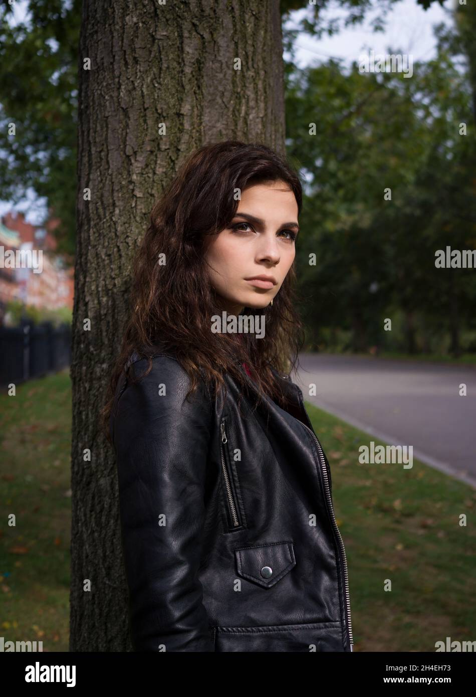 Ritratto di una giovane donna in una giacca di pelle nera in piedi davanti ad un albero Foto Stock