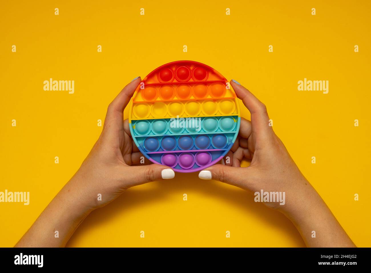 Trendy arcobaleno Pop IT antistress fidget giocattolo spingere pop in mani di bambino. Vista dall'alto, disposizione piatta. Foto Stock