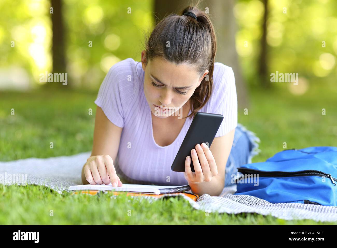 Studente concentrato che tiene appunti su carta di controllo smartphone che studia in un campus Foto Stock