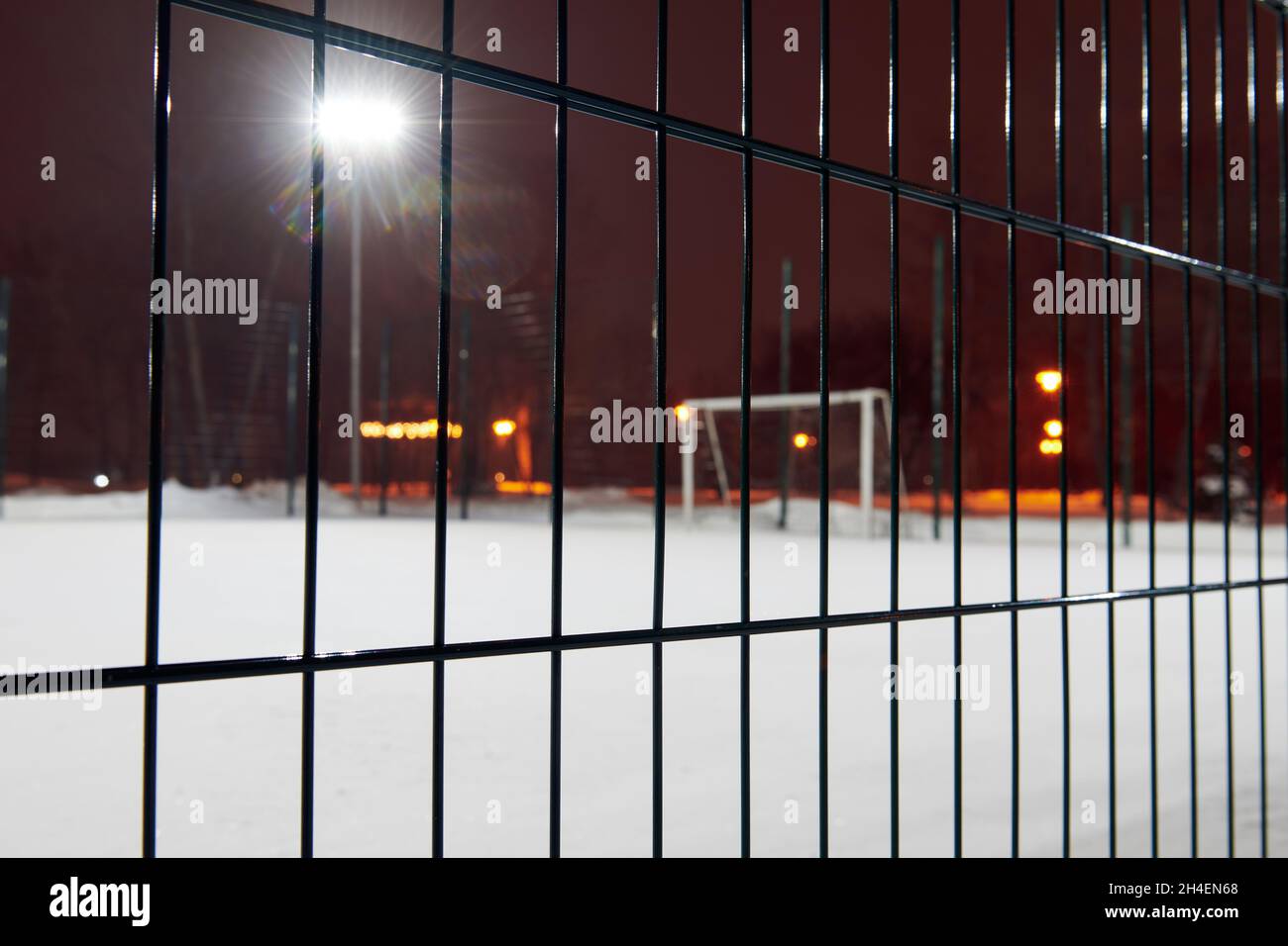 Campo da calcio coperto da uno spesso strato di neve. Vista attraverso la recinzione. Fuoco sulla recinzione. Foto sfocata. La partita notturna è annullata Foto Stock