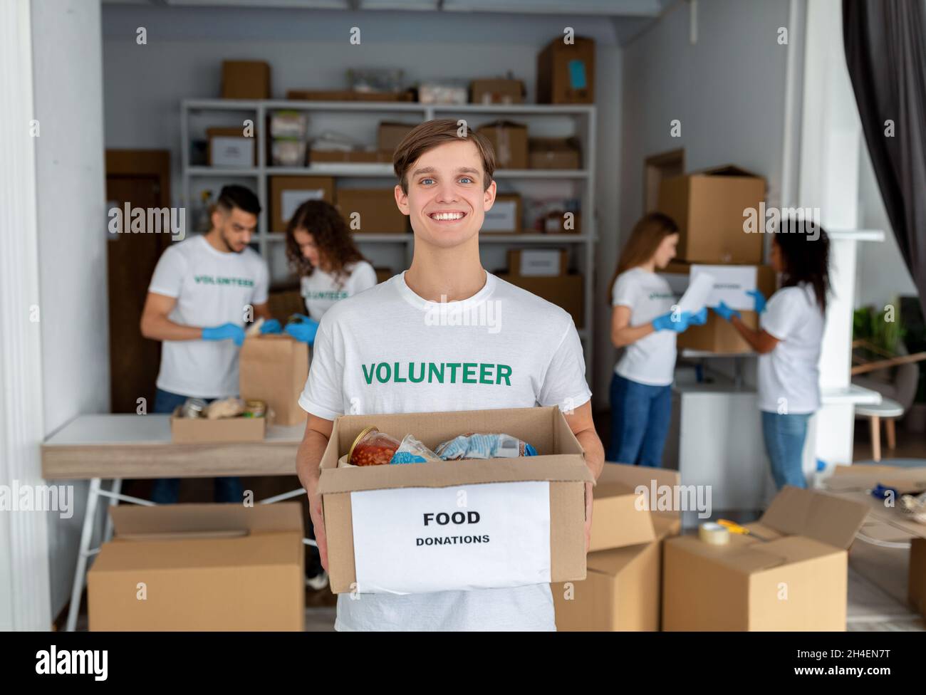 Felice giovane volontario maschile in uniforme custodia per la donazione, squadra che lavora insieme in ufficio di organizzazione caritativa Foto Stock