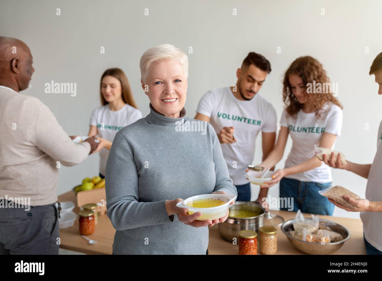 Concetto di donazione. Gruppo di volontariato che aiuta ad alimentare gli anziani con pasto gratuito. Donna anziana felice ha ricevuto zuppa calda Foto Stock