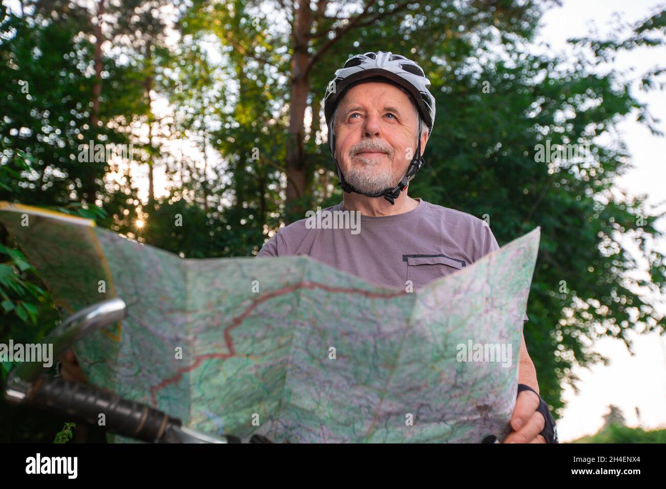 Uomo anziano che gode di ciclismo estivo nella foresta durante il tramonto incantevole, attivo pensionato Foto Stock