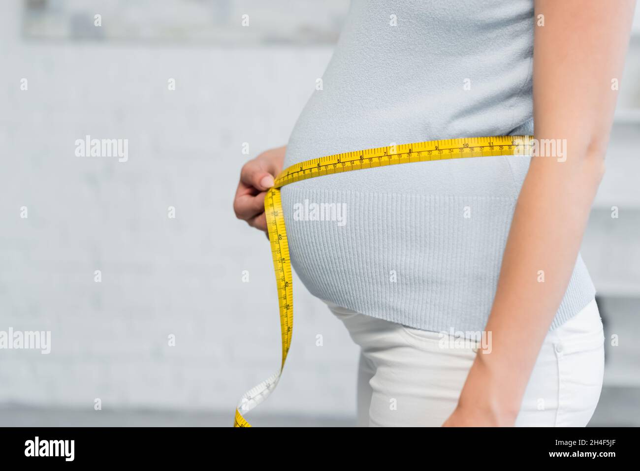 vista parziale della donna incinta che stima le dimensioni della pancia con nastro di misurazione Foto Stock