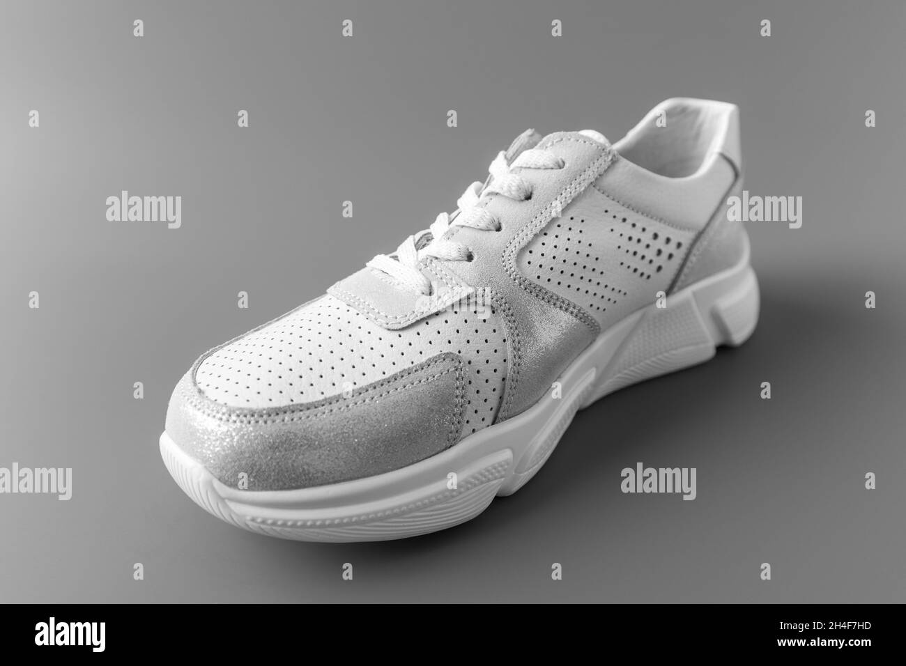 Una sneaker bianca in pelle da donna su sfondo grigio Foto Stock