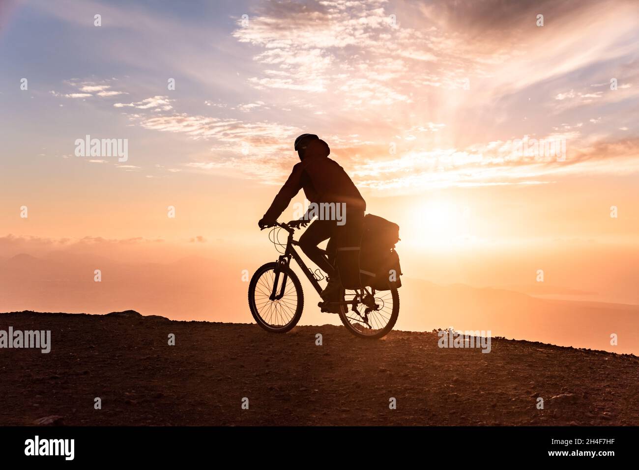 Il motociclista in mountain bike con zaino viaggia sullo sfondo dell'alba Foto Stock