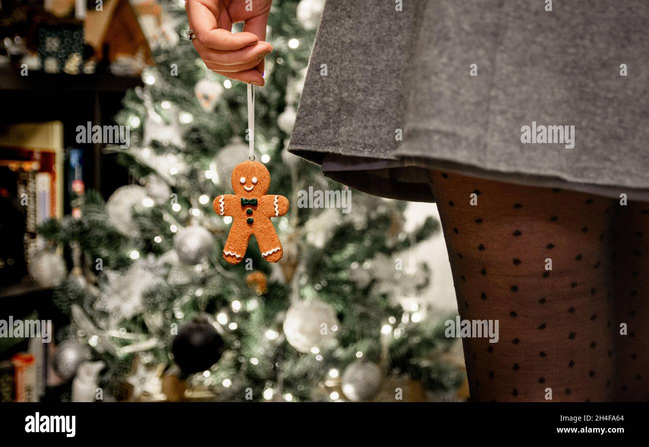 Foto ravvicinata della giovane donna che indossa gonna e pantyhose a pois polka, in piedi davanti all'albero di natale, tenendo l'ornamento uomo pan di zenzero Foto Stock