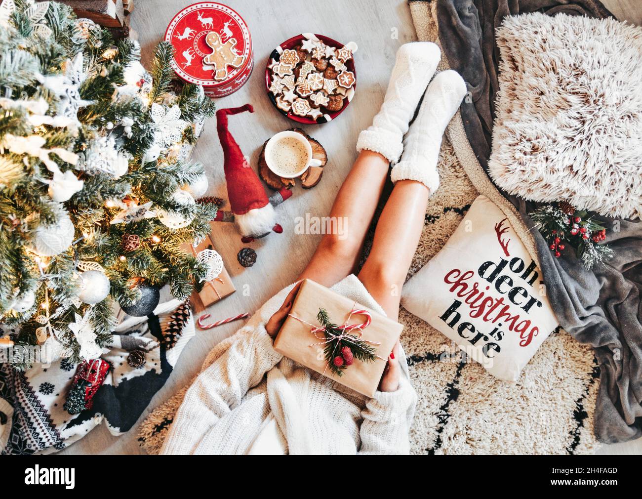 Foto in testa di donna che tiene regalo di natale, calzini caldi, seduta da albero di natale Foto Stock