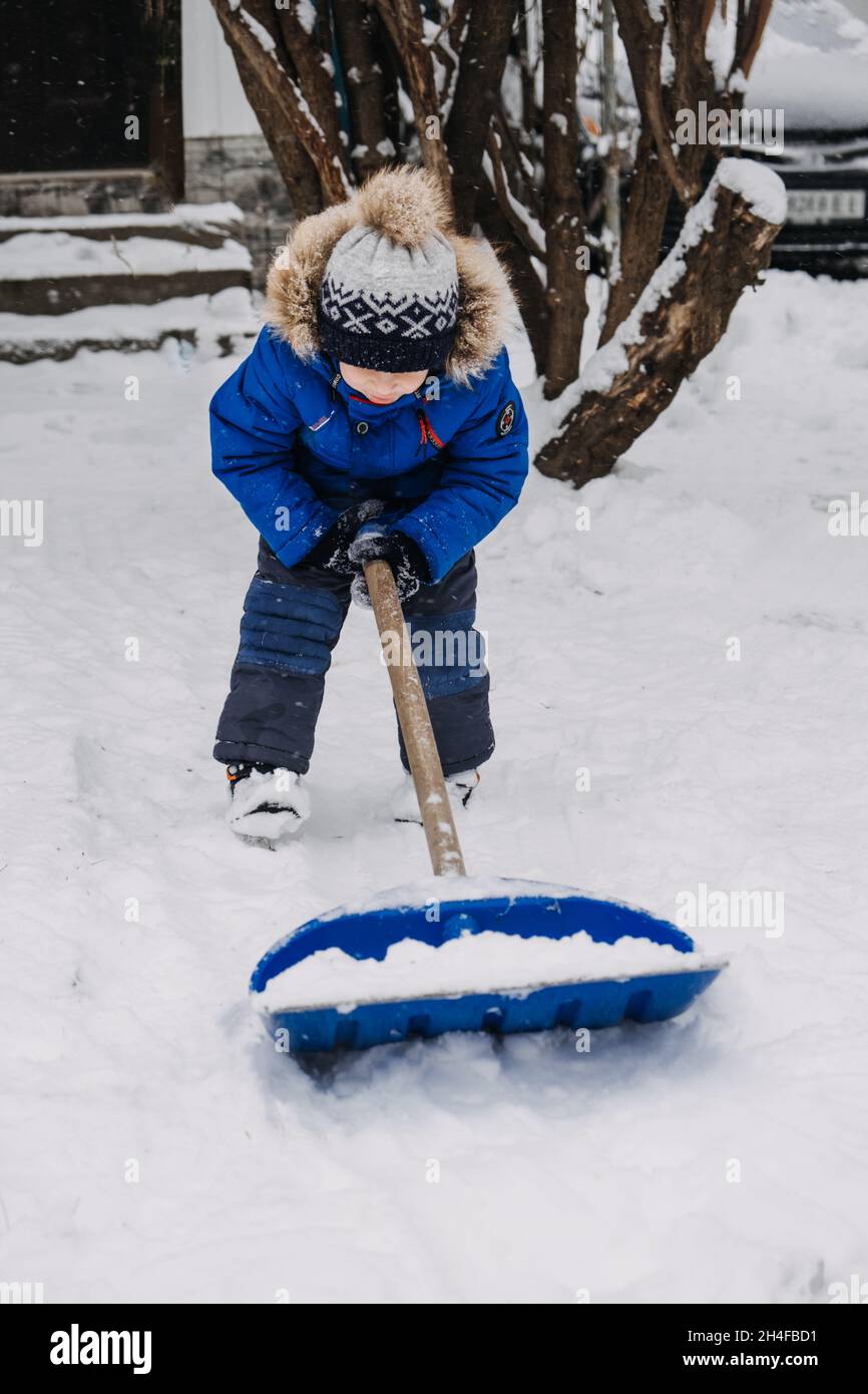 Ragazzino con una pala in mano rimuovere la neve nel cortile, rimozione della  neve. Il bambino in giacca blu pulisce la neve con la pala dopo la nevicata  Foto stock - Alamy