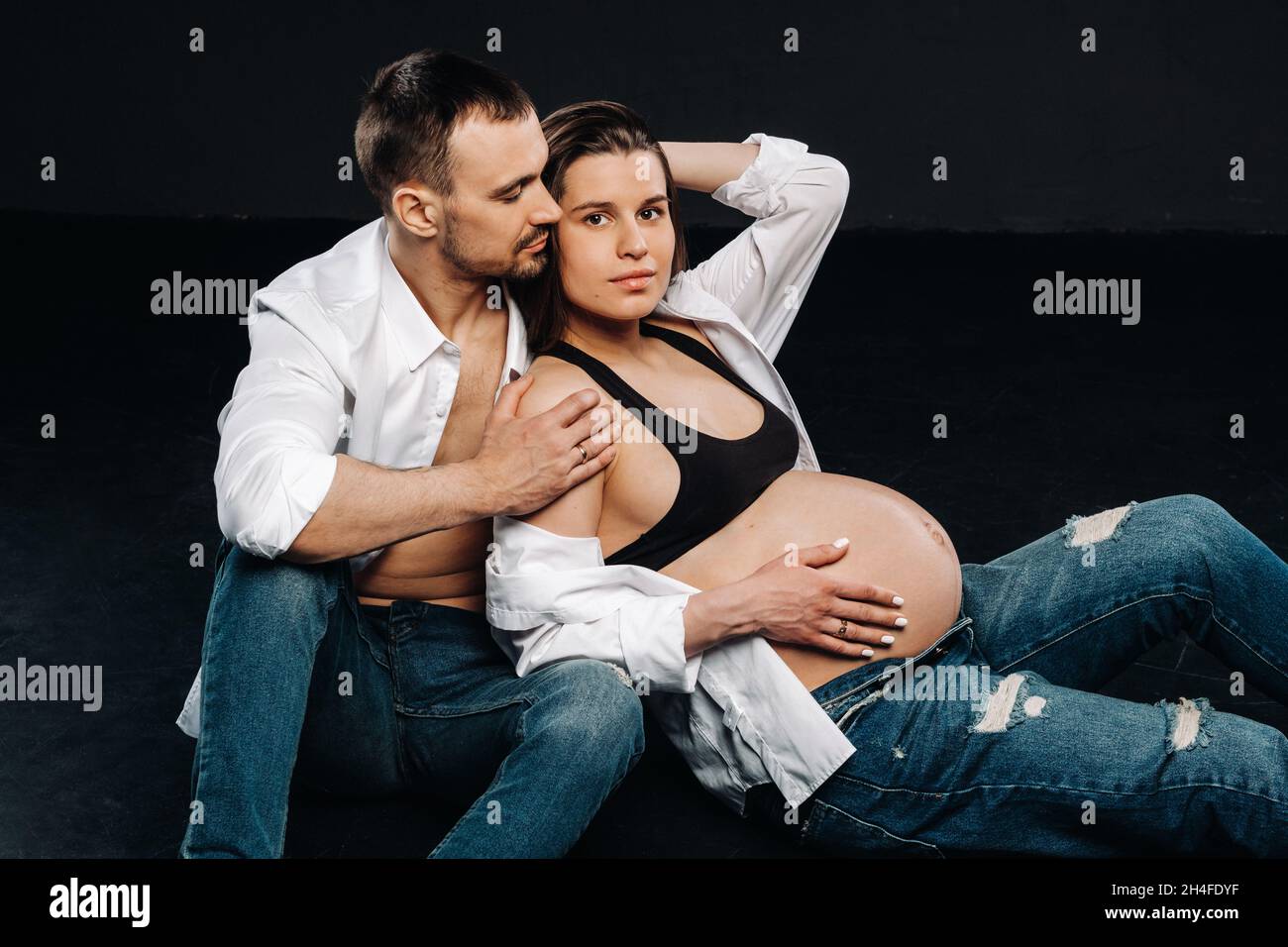 una donna incinta e un uomo in una camicia bianca e jeans in uno studio su  sfondo nero Foto stock - Alamy