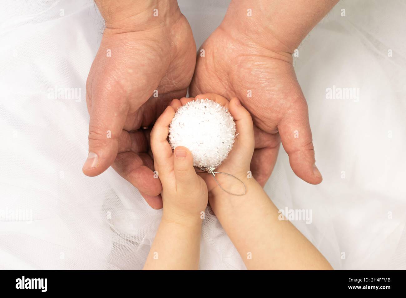 Il padre e la figlia che tengono una sfera decorativa bianca di Natale insieme con la cura e l'amore a decorare un albero di Natale. Capodanno e vigilia di natale Foto Stock