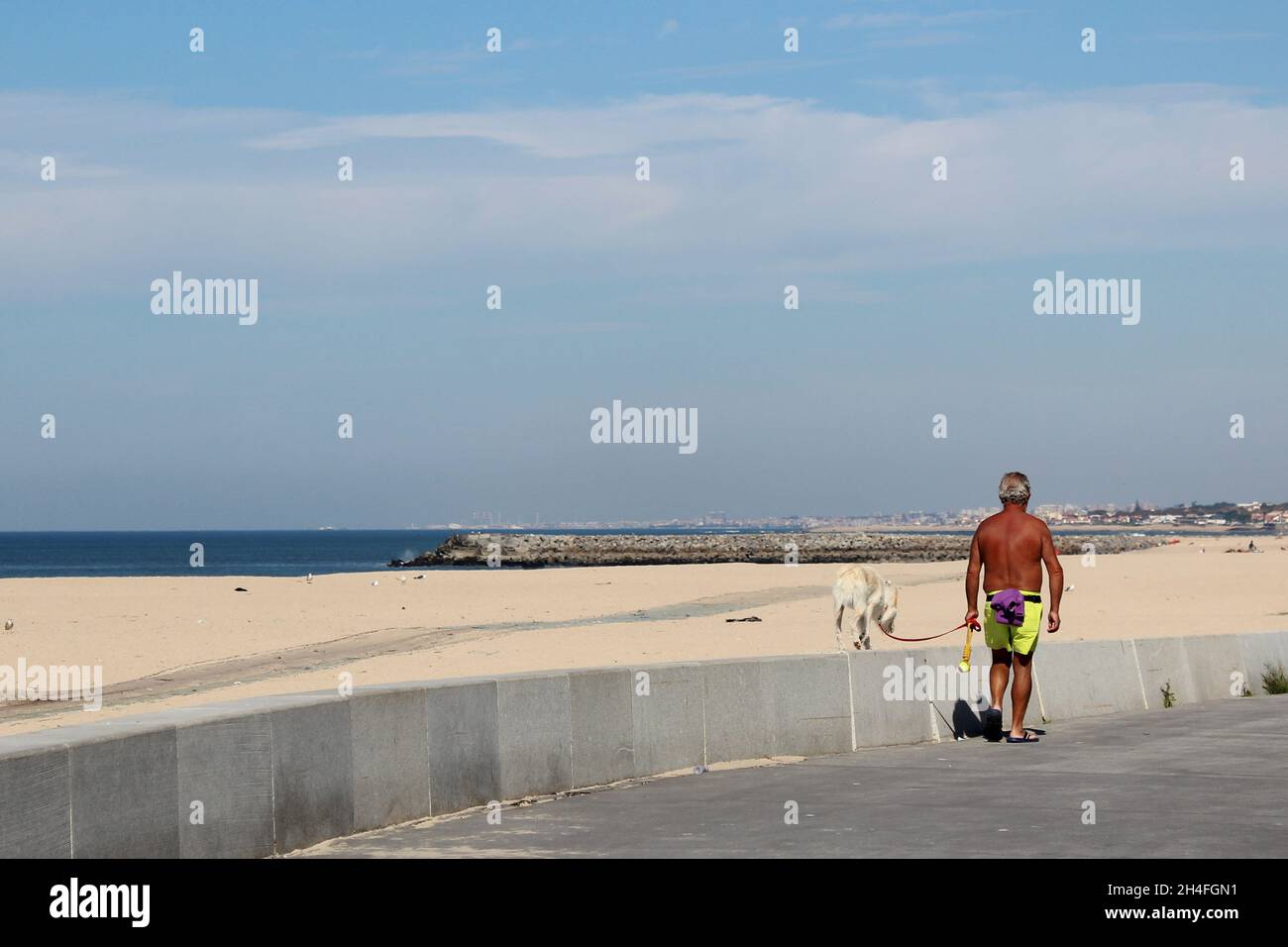 Ein braun gebrannter Mann (keine Erkennbarkeit) geht mit seinem Hund am Strand Gassi, Espinho, Portogallo. Foto Stock