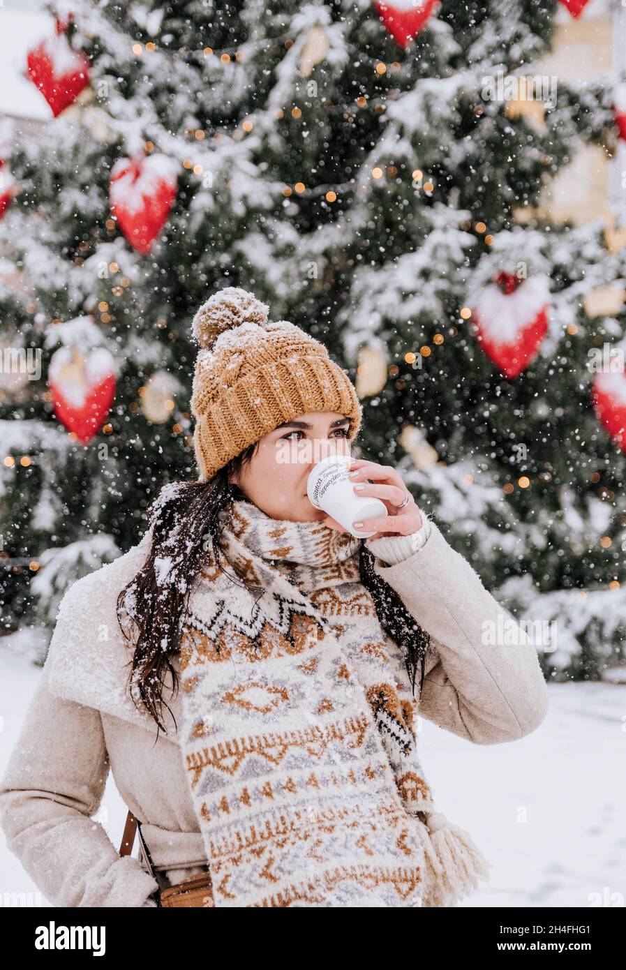 Ritratto di una giovane donna che indossa eleganti abiti invernali in città innevata, bevendo un caffè da portare via Foto Stock
