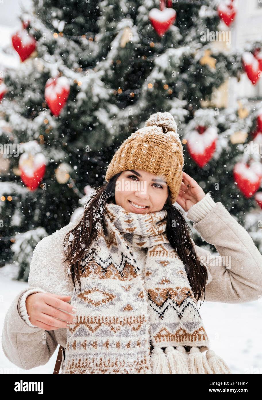 Ritratto di una giovane donna che indossa abiti invernali eleganti, in piedi davanti all'albero di natale in una giornata nevosa in città Foto Stock