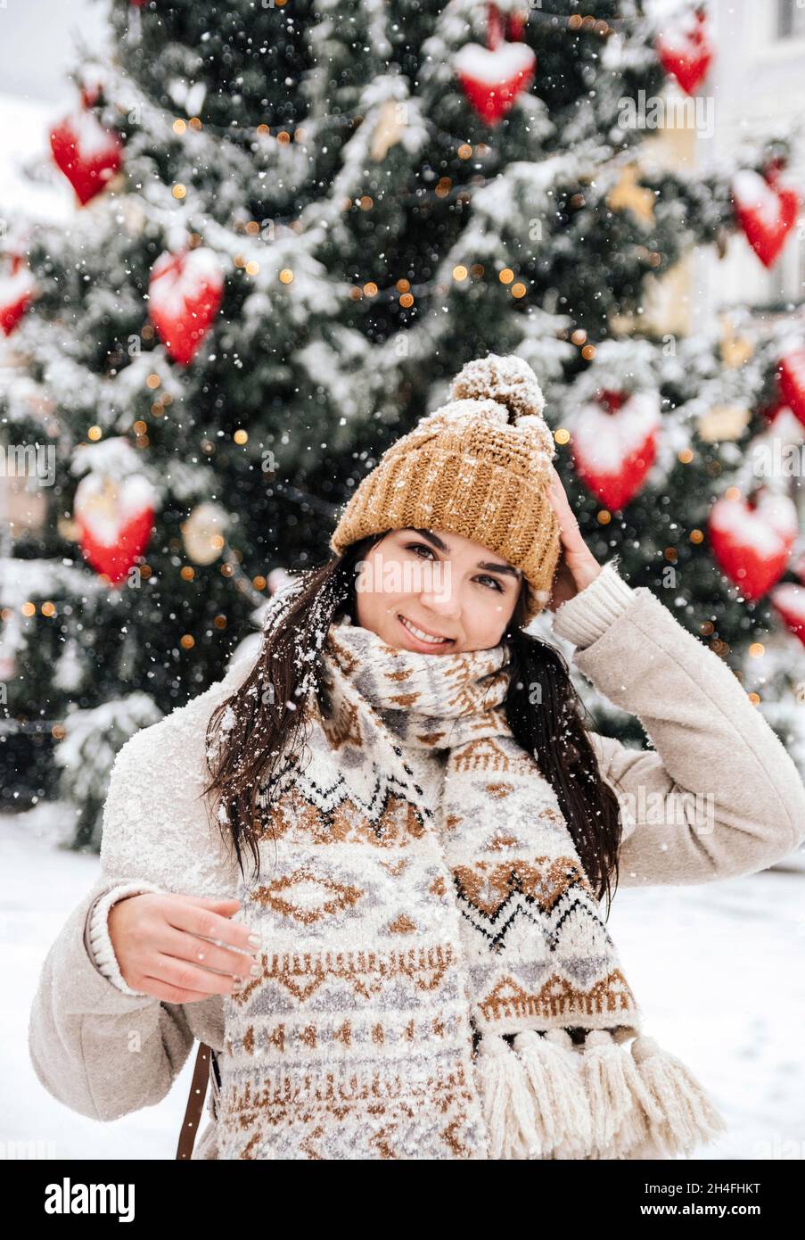 Ritratto di una giovane donna che indossa abiti invernali eleganti, in piedi davanti all'albero di natale in una giornata nevosa in città Foto Stock