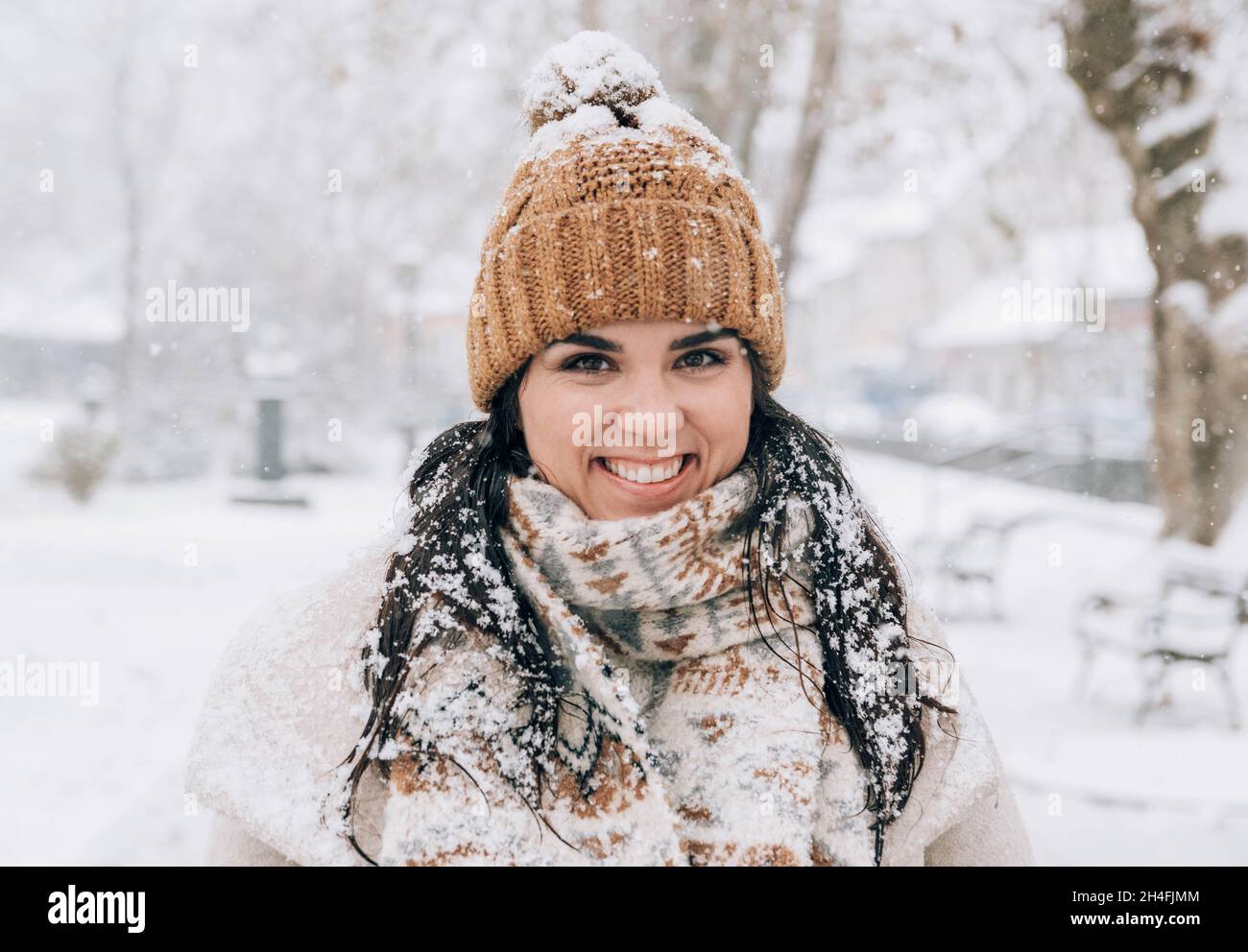 Ritratto di una giovane donna carina con fiocchi di neve in capelli, in piedi nel parco nevoso. Foto Stock