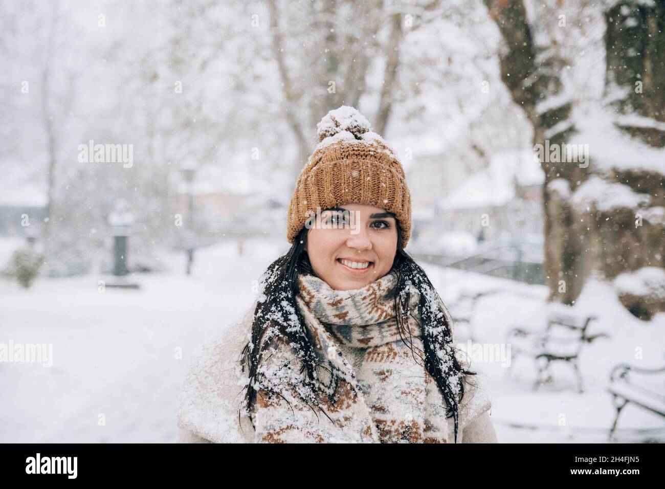 Ritratto di una giovane donna carina con fiocchi di neve in capelli, in piedi nel parco nevoso. Foto Stock