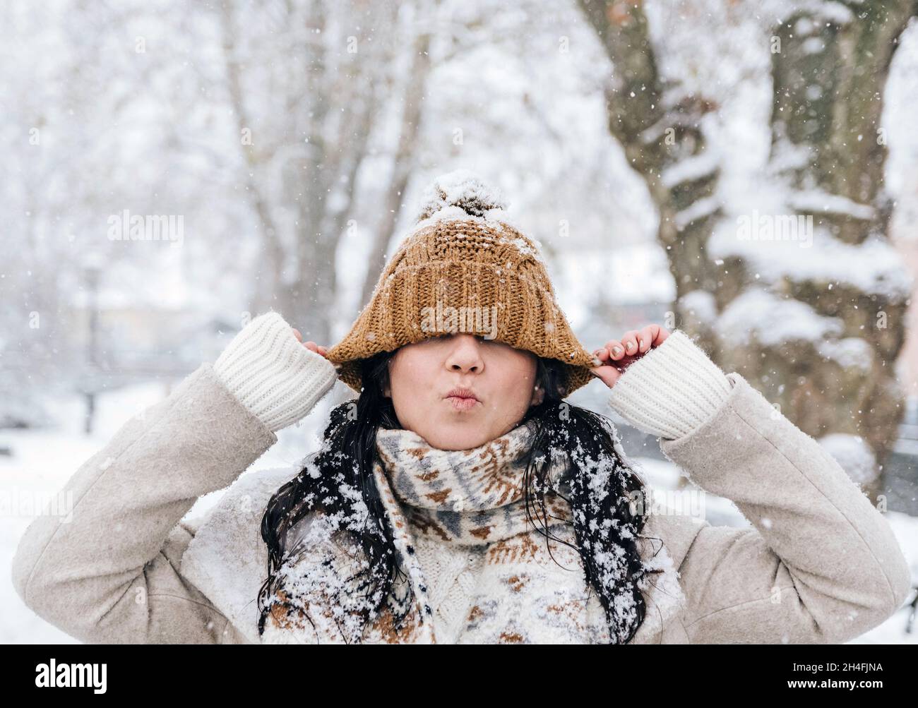 Ritratto di bella giovane donna in abiti invernali tirando il cappello giù sopra gli occhi. Foto Stock