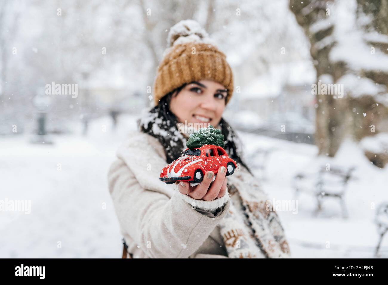 Ritratto di una bella giovane donna che tiene auto rossa giocattolo in parcheggio in una giornata nevosa in inverno. Foto Stock