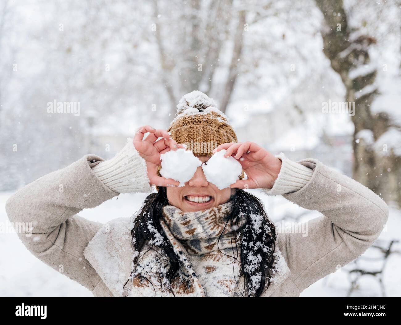 Ritratto invernale di bella giovane donna che tiene le palle di neve davanti ai suoi occhi in idilliaco parco nevoso Foto Stock