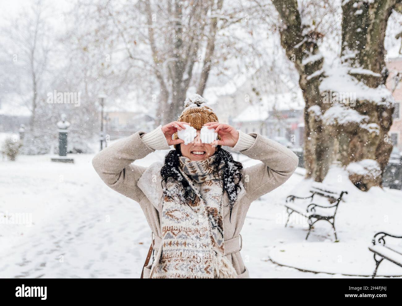 Ritratto invernale di bella giovane donna che tiene le palle di neve davanti ai suoi occhi in idilliaco parco nevoso Foto Stock