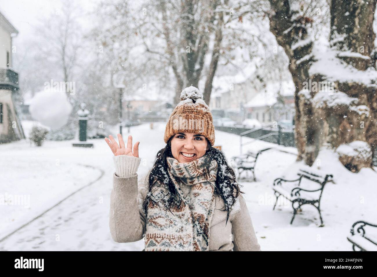 Ritratto di bella giovane donna in abiti invernali in piedi nel parco nevoso, gettando palla di neve Foto Stock