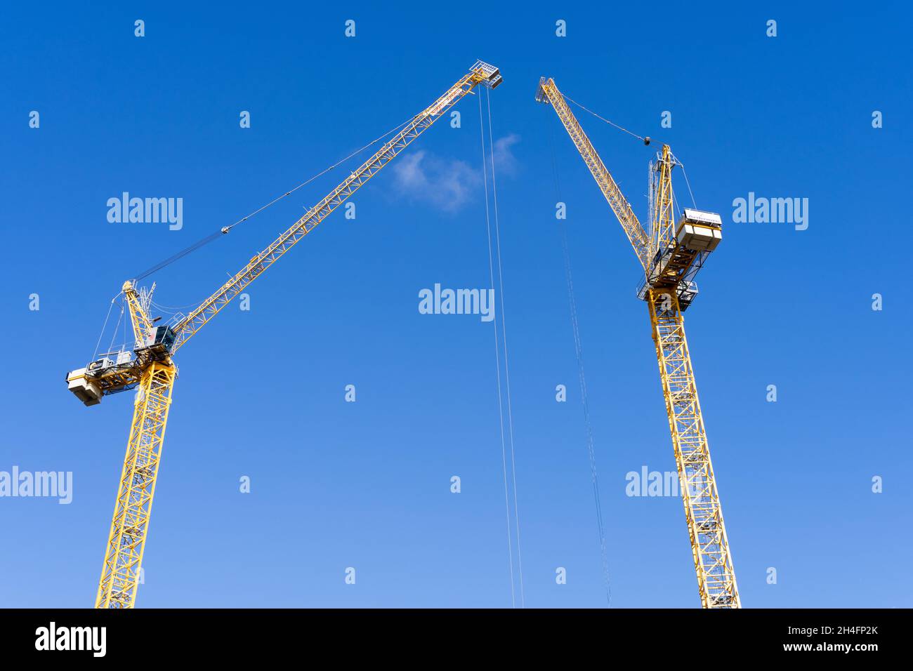 Due gru gialle da costruzione che si estendono nel cielo blu in un sito di sviluppo immobiliare a Greenwich, Londra, in una giornata di sole, Regno Unito Foto Stock