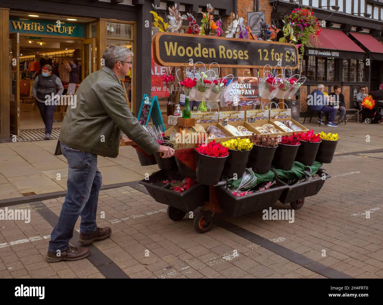 Un venditore di strada che spinge un barrow di fiori, rose di legno, e biscotti lungo la strada. Foto Stock