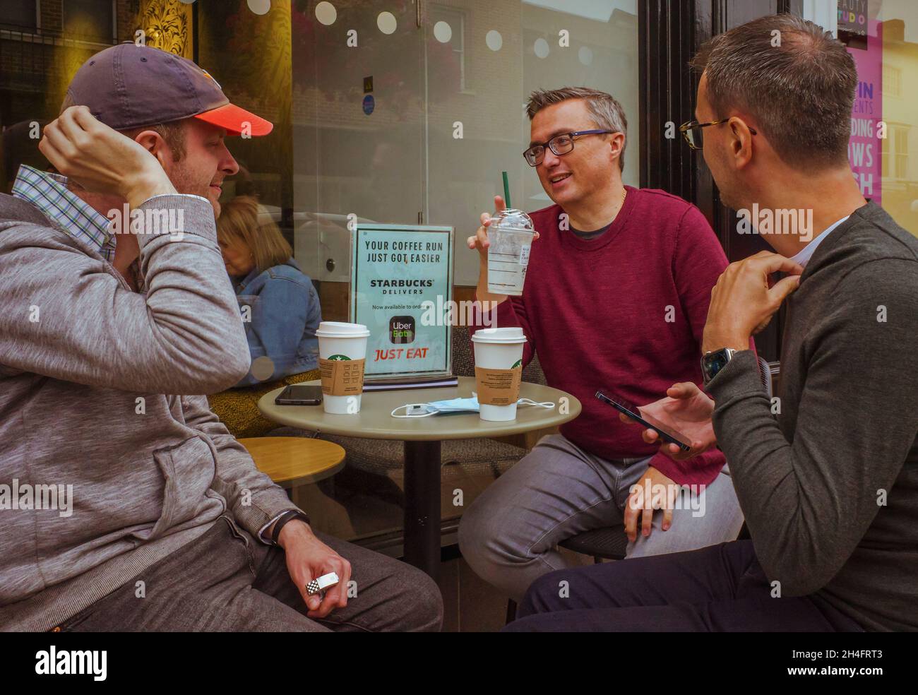 Un gruppo di amici maschi seduti a un tavolo esterno che parlano e si godono una tazza di caffè. Foto Stock