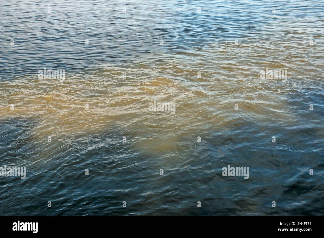 L'acqua arancione sporca proveniente dal gasdotto si mescola con l'acqua del fiume. Bordo chiaro tra due diversi flussi d'acqua. Tema dell'inquinamento ambientale. Foto Stock