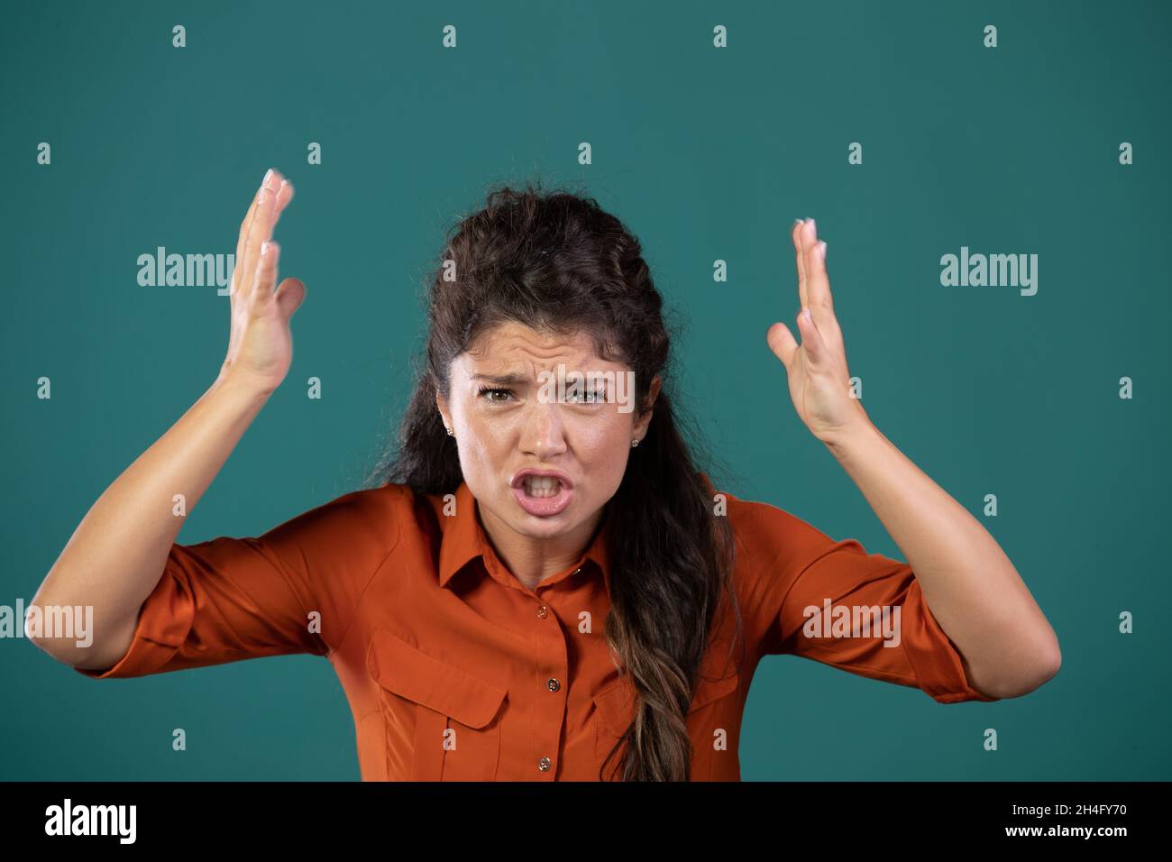 Ritratto di donna arrabbiata urlando, tenendo le mani in aria, su sfondo blu in studio Foto Stock